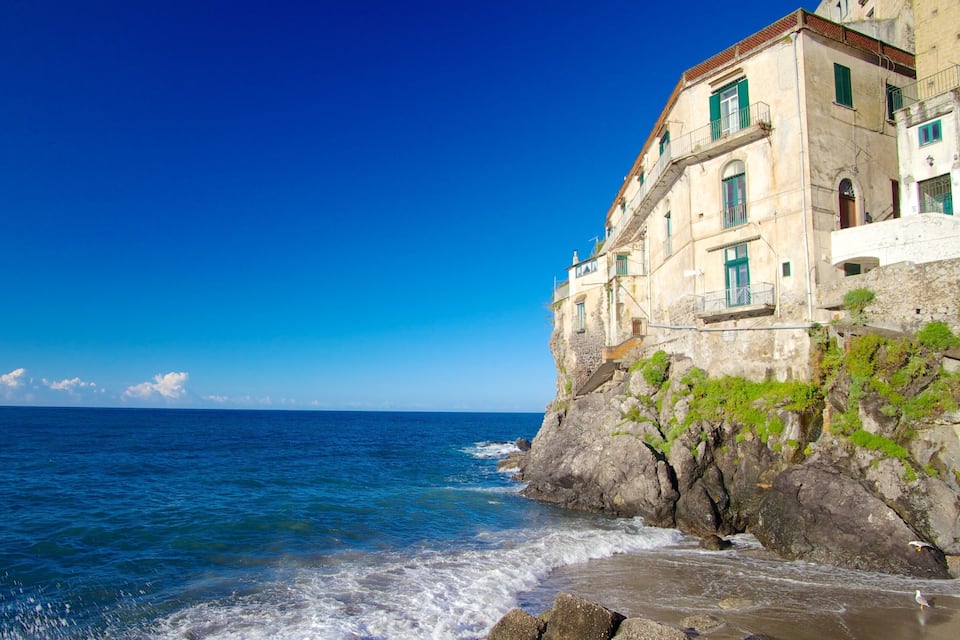 Un edificio frente al mar con fachada de piedra y contraventanas verdes.