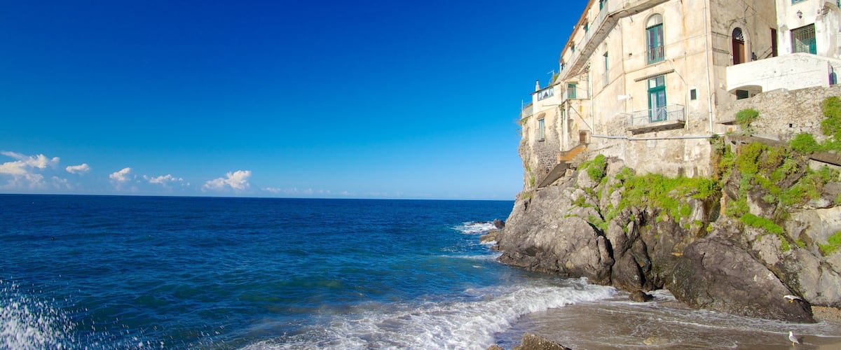 A coastal building with a stone facade and green shutters, overlooking the sea.