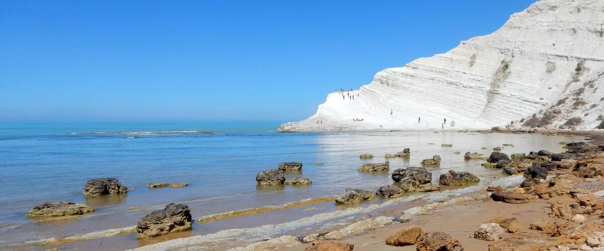 A coastal landscape with white cliffs, clear blue sea, and rocky shoreline.