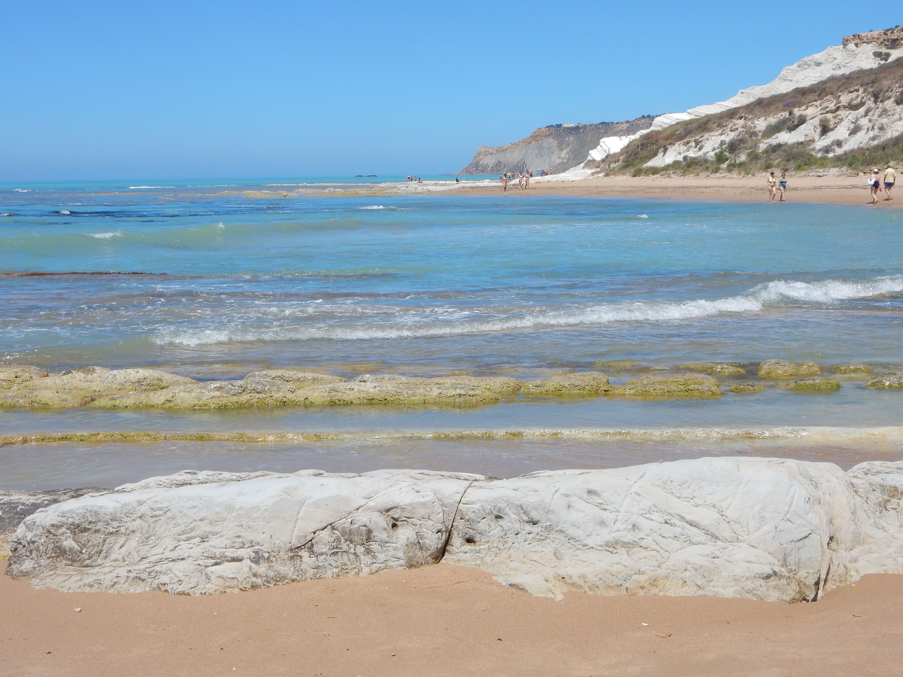 A beach with clear blue water, rocky formations, and a sandy shore.