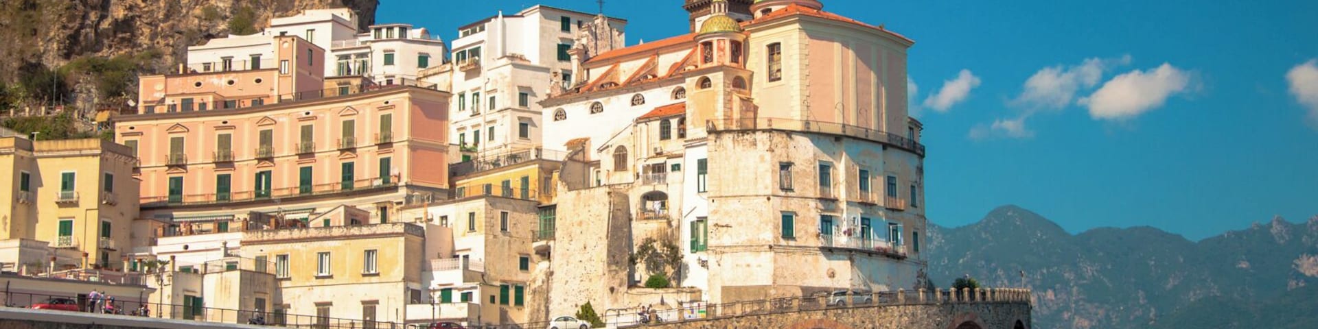 Un pueblo costero con edificios históricos, una iglesia destacada de cúpula verde y una animada zona de playa con sombrillas y gente.