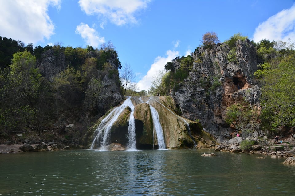 A waterfall cascading into a river surrounded by rocky cliffs and dense foliage.