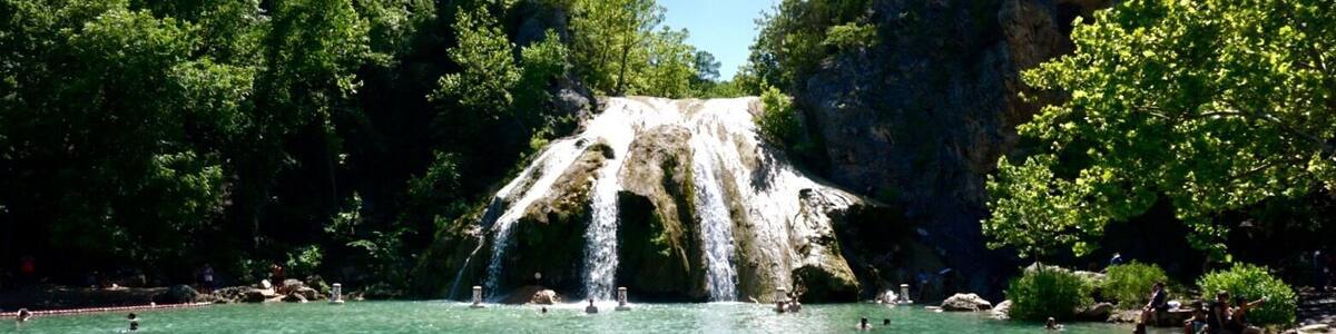 Une cascade se jetant dans un bassin d’eau turquoise et limpide, entouré d’une végétation luxuriante et de falaises rocheuses.