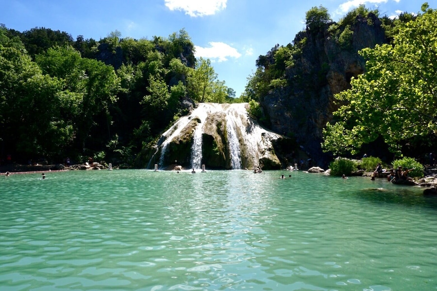 A waterfall cascading into a clear turquoise pool surrounded by lush greenery and rocky cliffs.