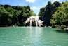 A waterfall cascading into a clear turquoise pool surrounded by lush greenery and rocky cliffs.