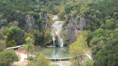 Una cascada fluye a un río rodeado de un bosque denso y acantilados rocosos.