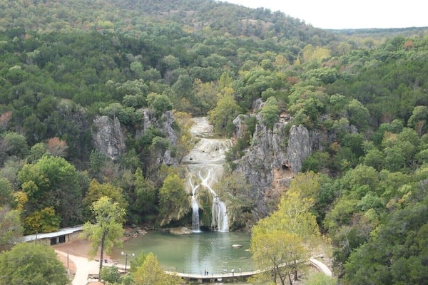 Ein Wasserfall stürzt in einen Fluss, umgeben von dichtem Wald und steilen Felswänden.