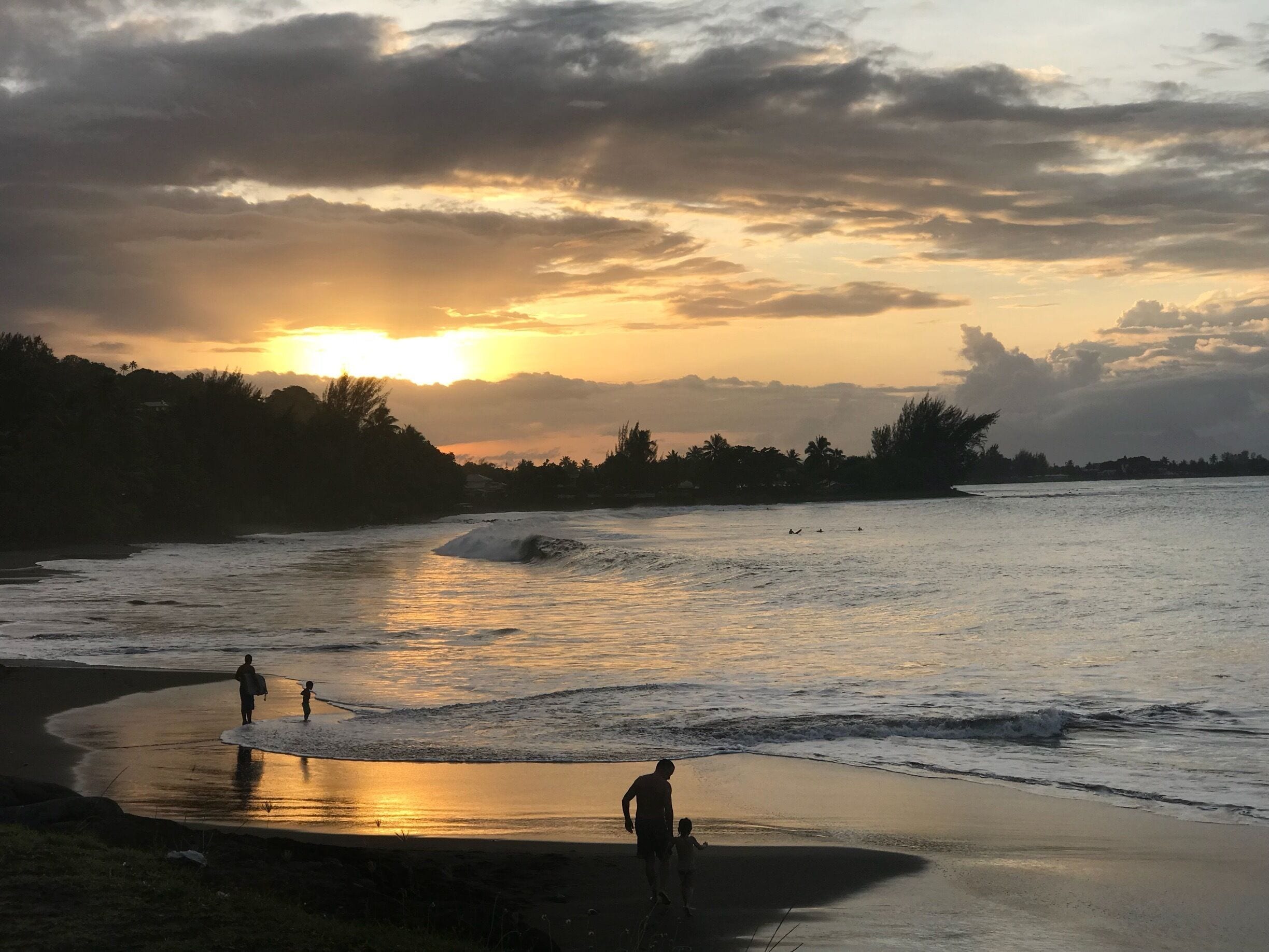 A sunset over a beach with waves and silhouettes of people.