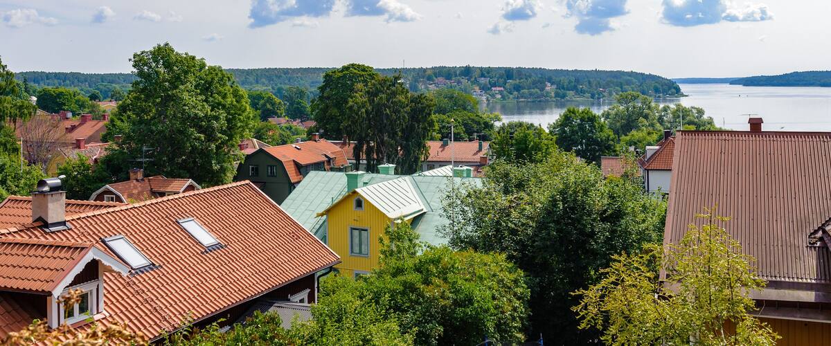 A town with red-tiled roofs, green trees, and a lake in the distance.