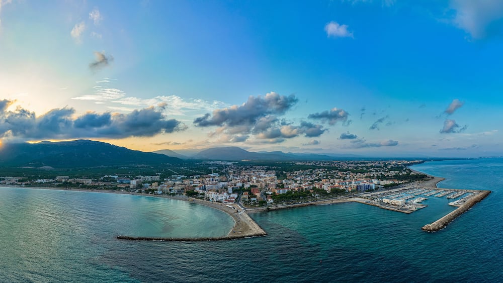 A coastal city with a marina, mountains in the background, and a clear sky.