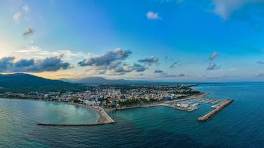 A coastal city with a marina, mountains in the background, and a clear sky.