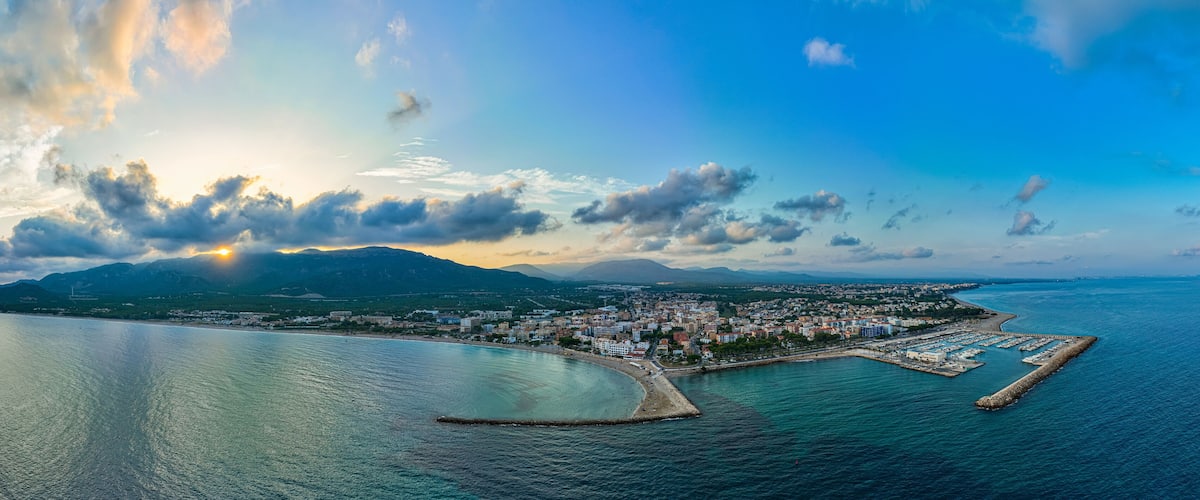 A coastal city with a marina, mountains in the background, and a clear sky.