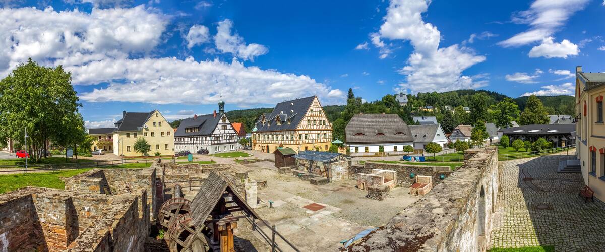 A historic town with medieval architecture, cobblestone streets, and a large water wheel.