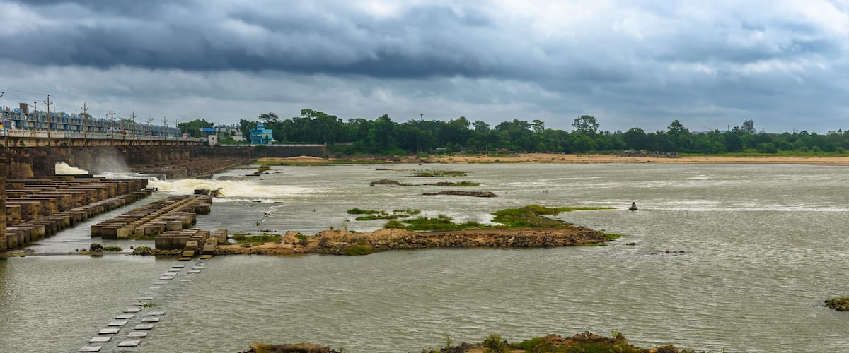 A river with a dam, rocky outcrops, and a bridge.
