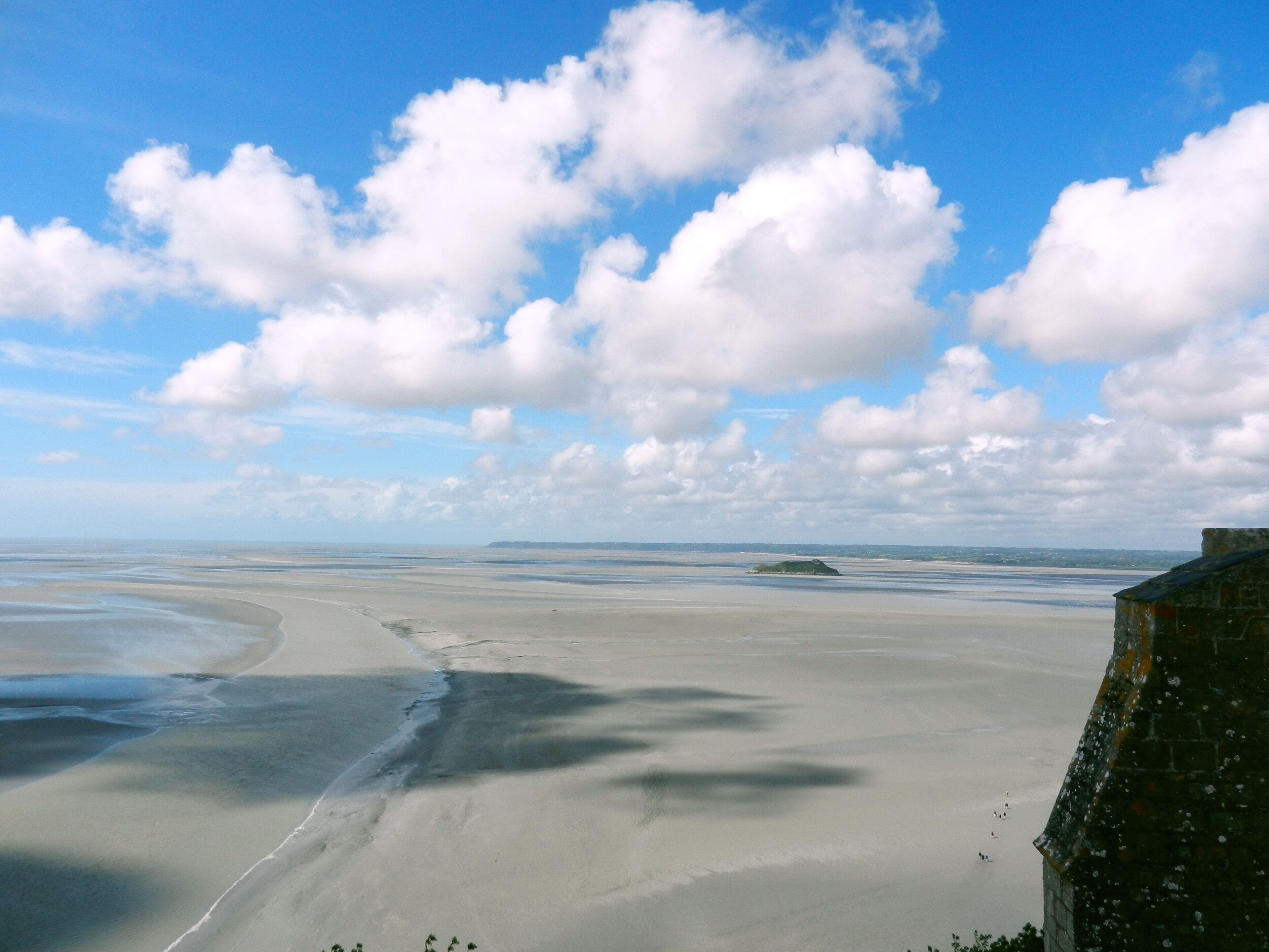 Un paisaje costero con una playa arenosa, un edificio de piedra y una isla distante.