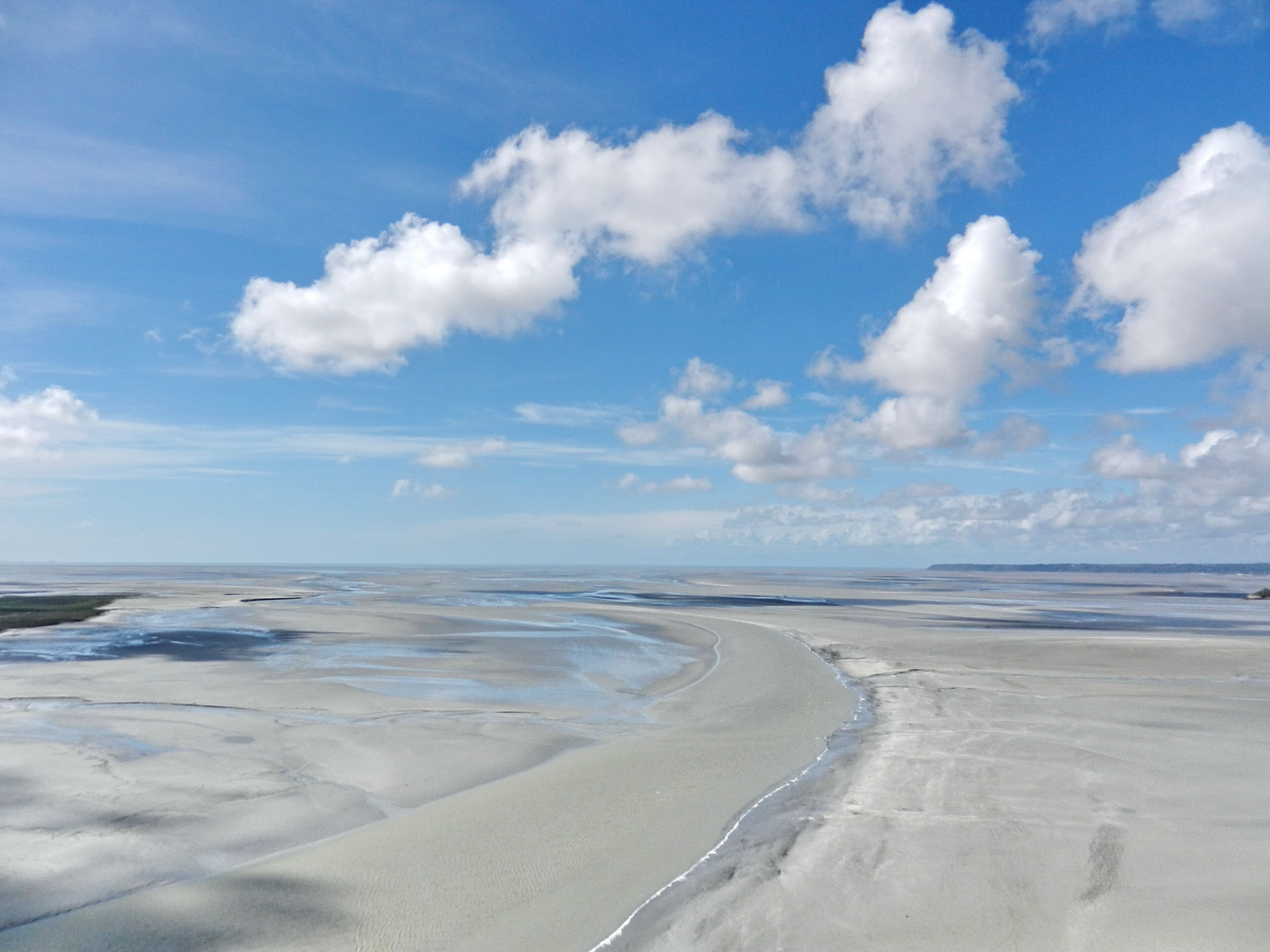 Paisaje costero con dunas de arena y un cielo azul despejado con nubes dispersas.