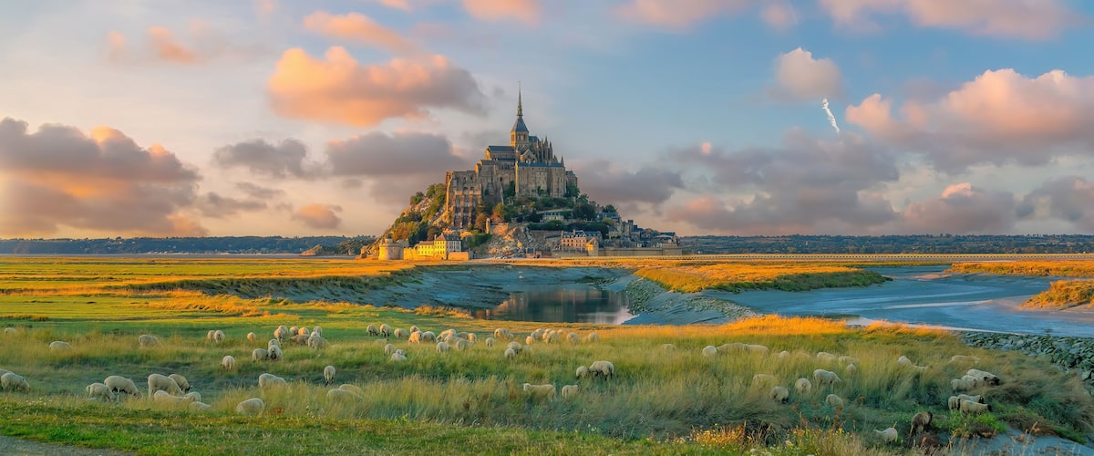 A historic castle on a hill, surrounded by a river and grazing sheep.