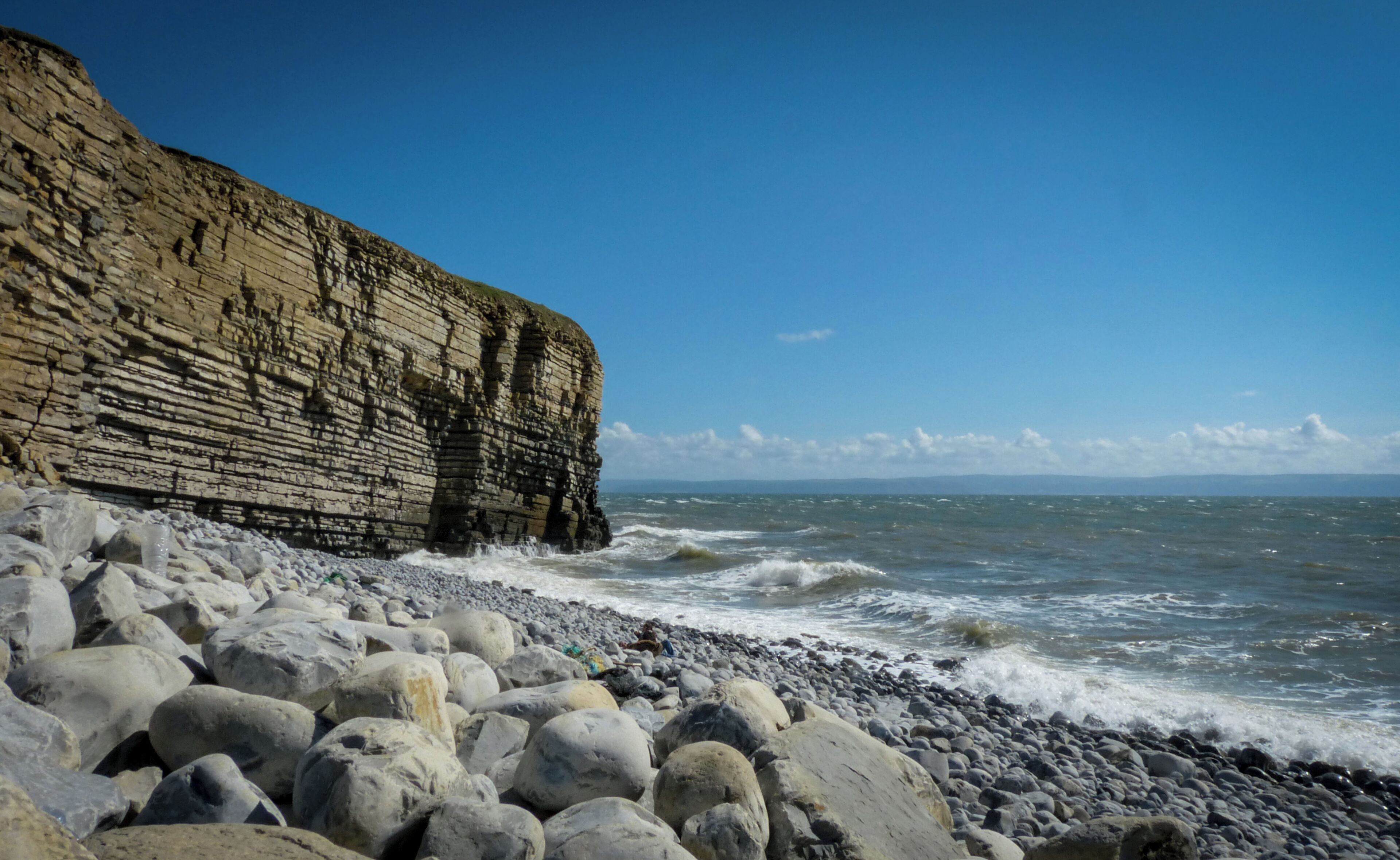 A rocky coastline with layered cliffs and waves crashing onto the shore.