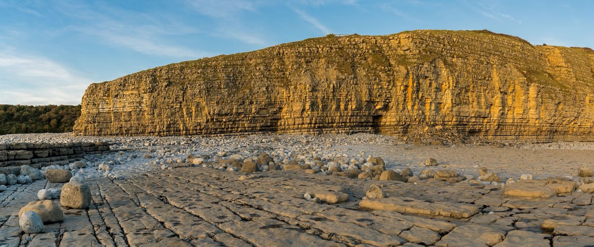 A large rock formation with layered strata and a rocky foreground.