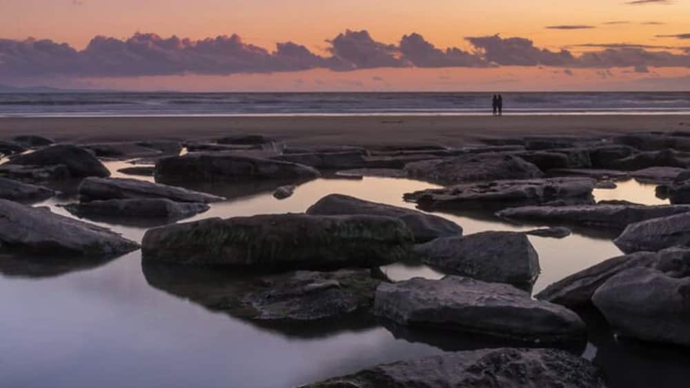 Un rivage rocheux bordé d’une eau calme qui reflète le ciel au coucher du soleil.