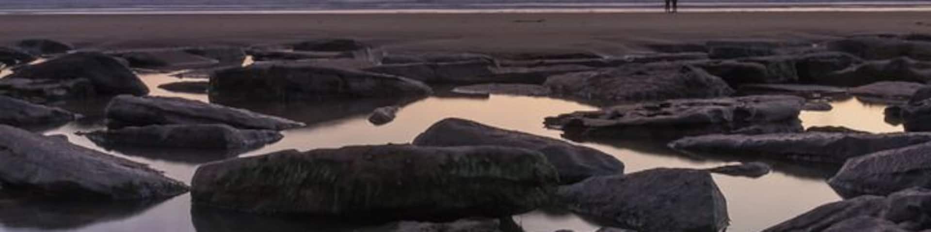 A rocky shoreline with calm water reflecting the sky during sunset.