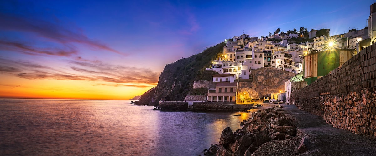 A coastal town at sunset with buildings on a cliff overlooking the sea.