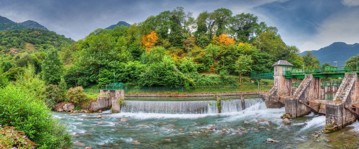 A river flowing through a lush valley with a small waterfall and a bridge.