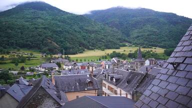 A village with traditional houses and a church with a tall spire, surrounded by lush green hills.