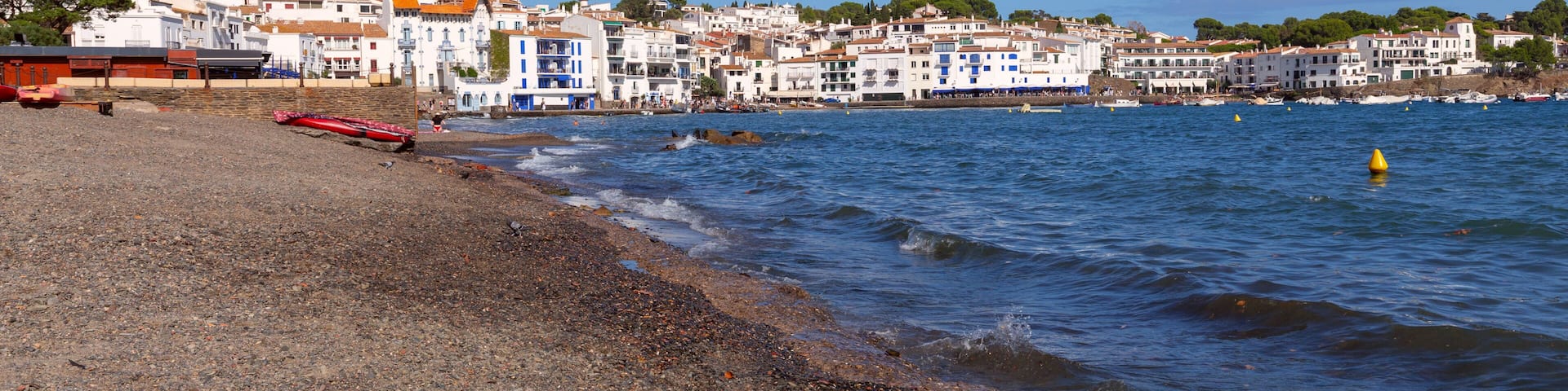Pebble beach and waterfront houses in Cadaques on sunny day, Catalonia, Spain