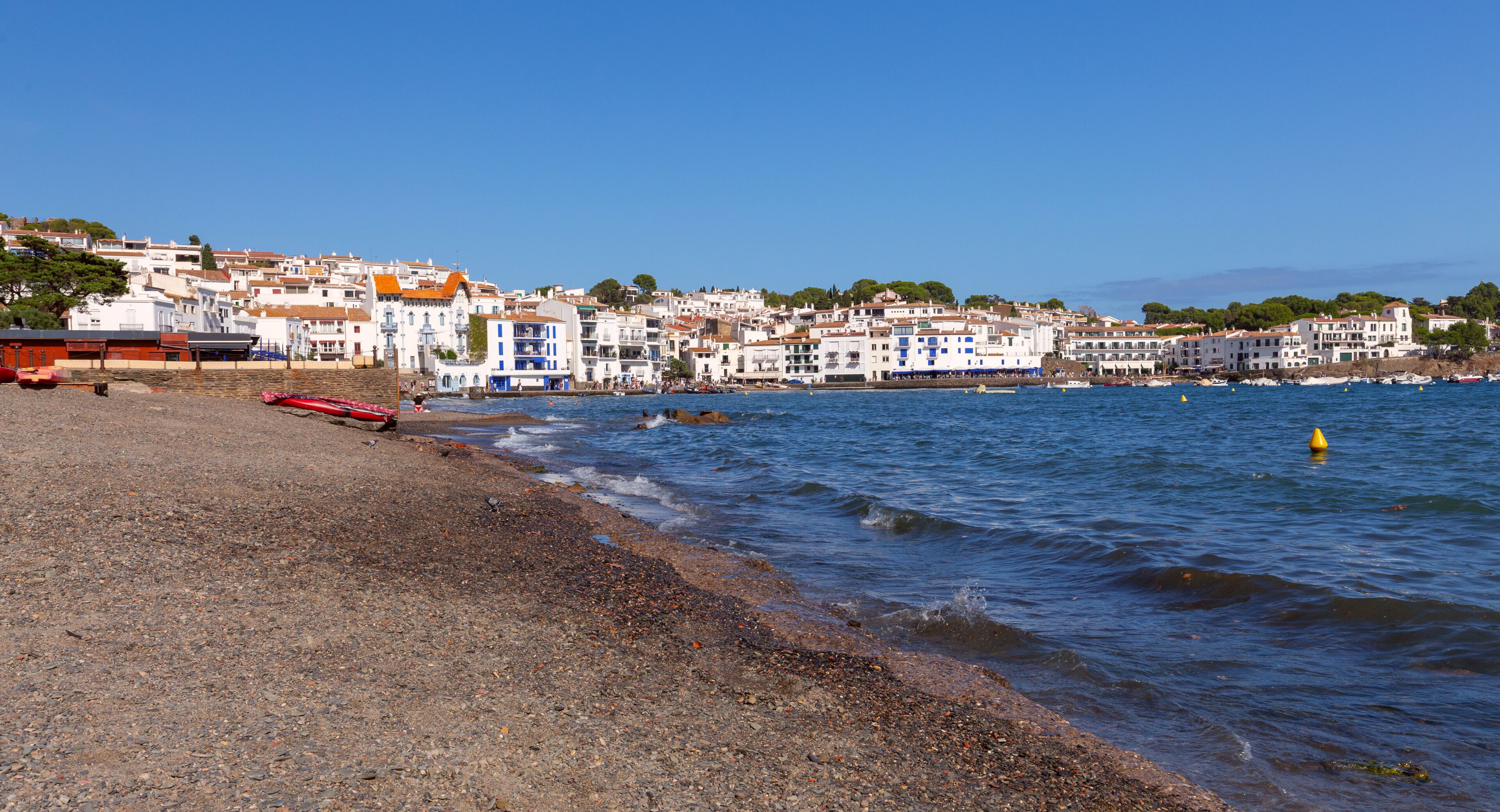 A coastal town with white buildings, a pebble beach, and calm sea.