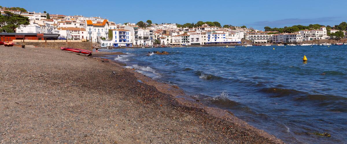 A coastal town with white buildings, a pebble beach, and calm sea.