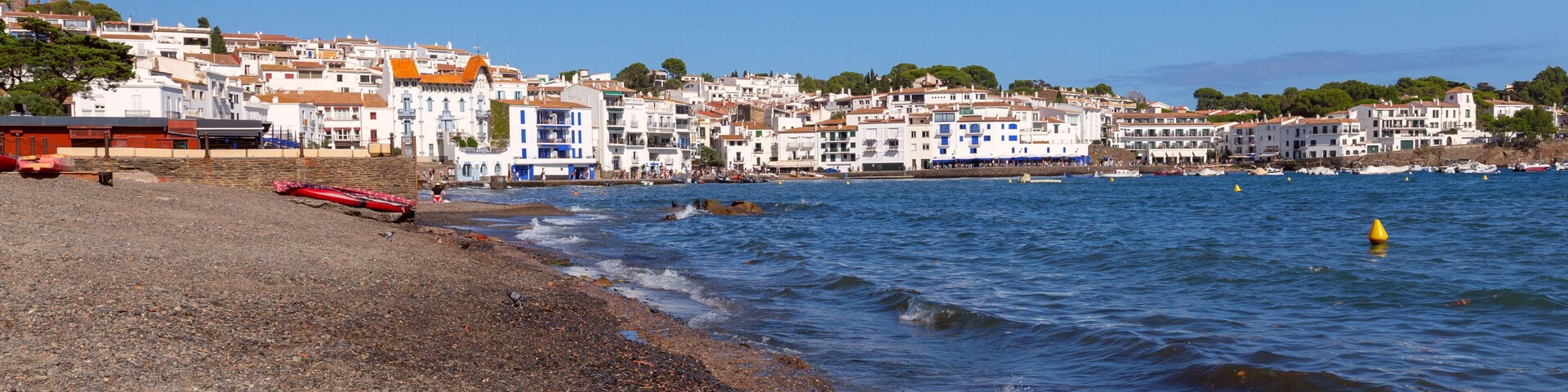 A coastal town with white buildings, a pebble beach, and calm sea.