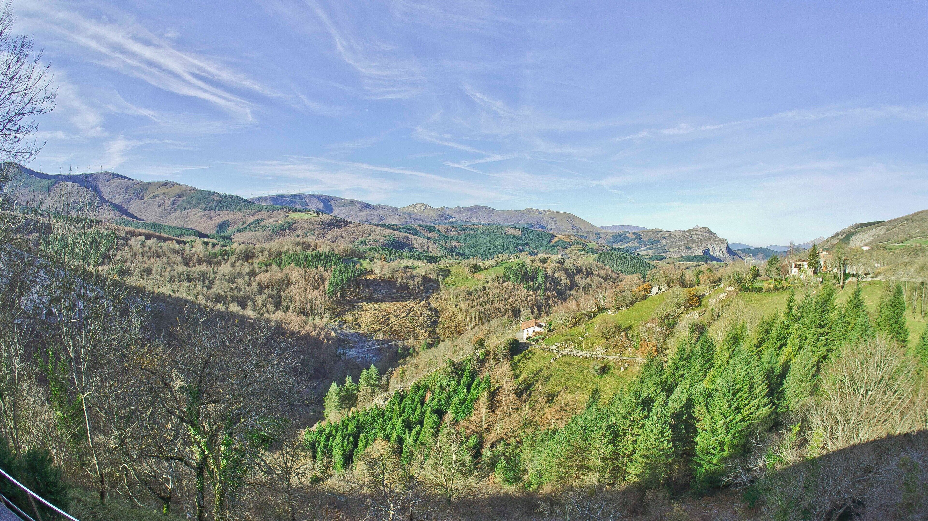 A valley with a river, dense forests, and distant mountains under a clear sky.