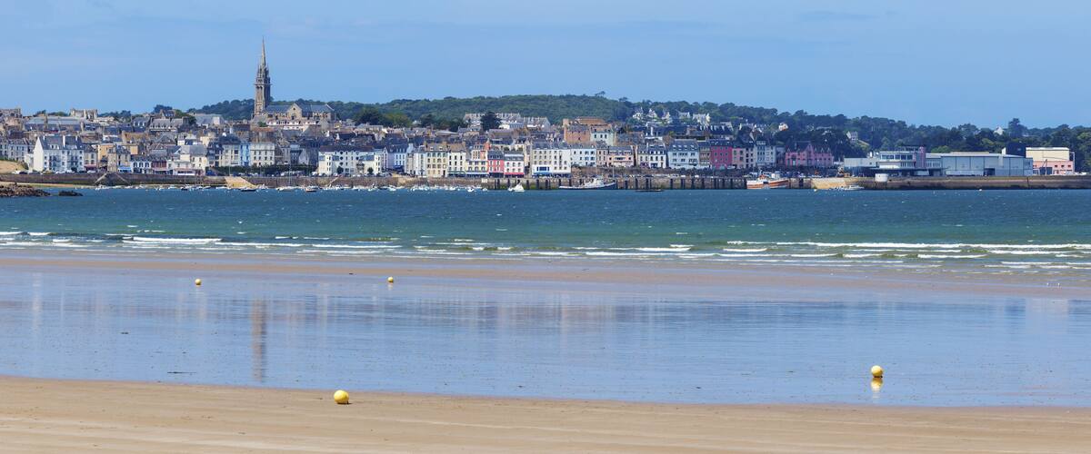 A coastal town with a prominent church tower, a sandy beach, and a harbor with boats.