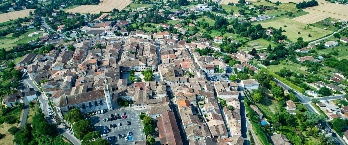 An aerial view of a historic town with narrow streets, old buildings, and surrounding green fields.