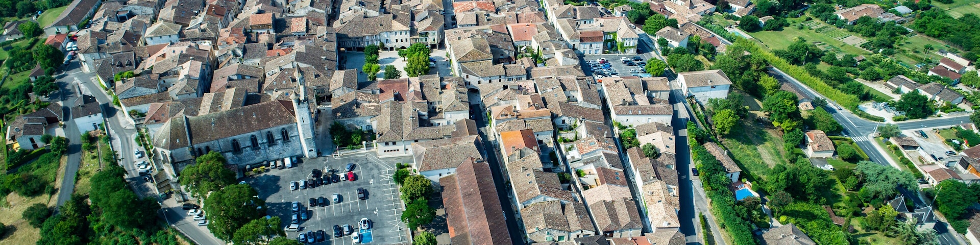 An aerial view of a historic town with narrow streets, old buildings, and surrounding green fields.