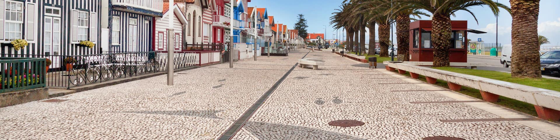 A cobblestone street lined with colorful buildings, palm trees, and a clear blue sky.