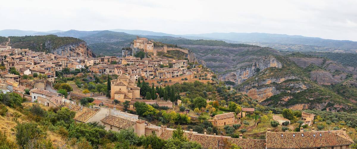 A historic town nestled in a valley with terraced buildings and a prominent castle on a hill.