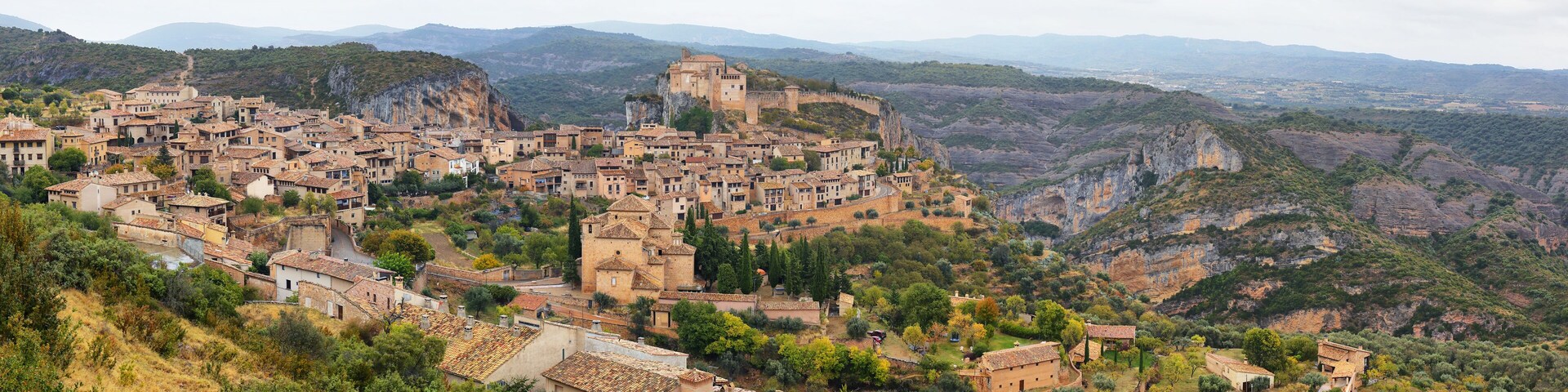 A historic town nestled in a valley with terraced buildings and a prominent castle on a hill.