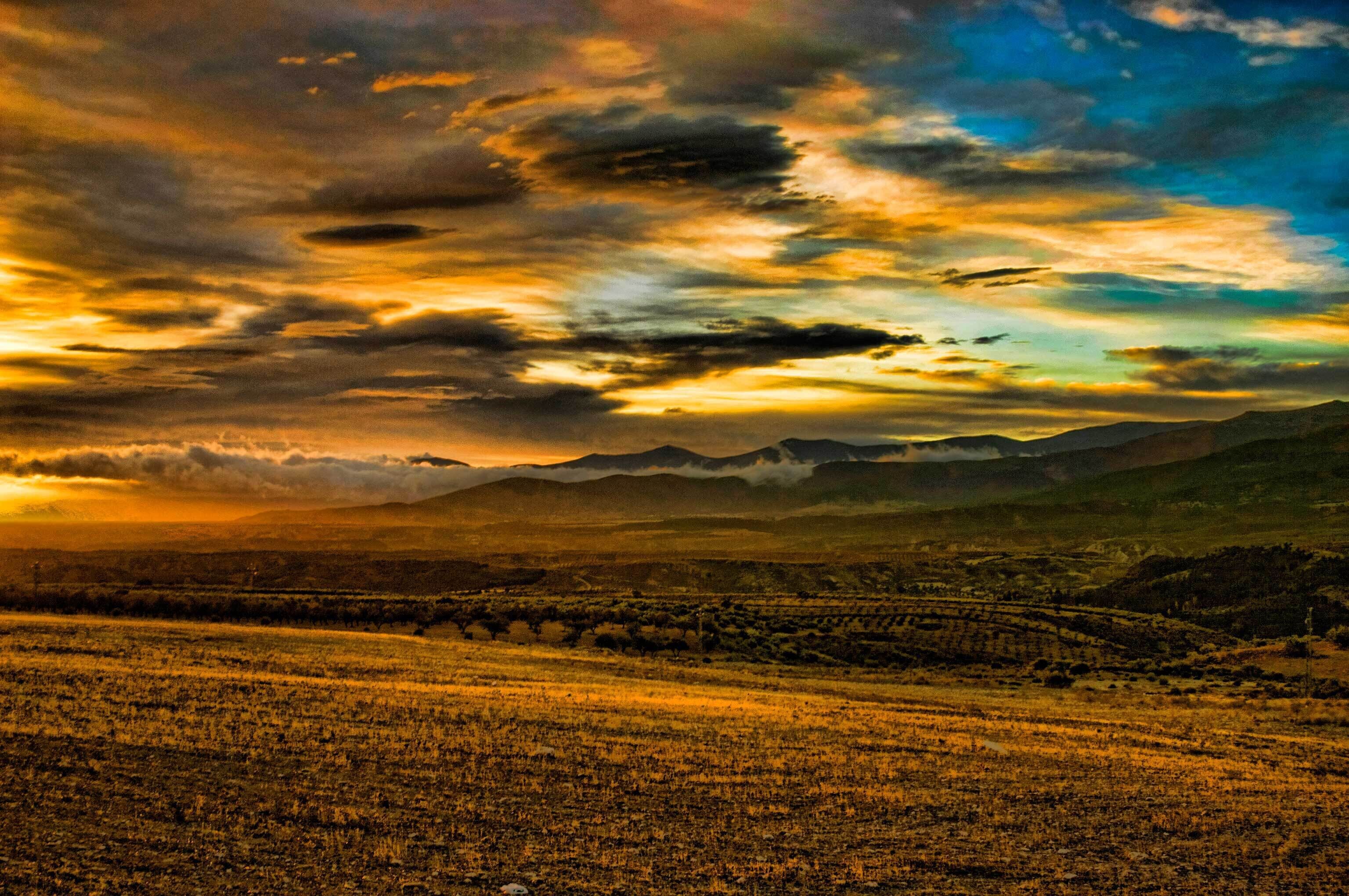 A sunset over a mountainous landscape with a field in the foreground.