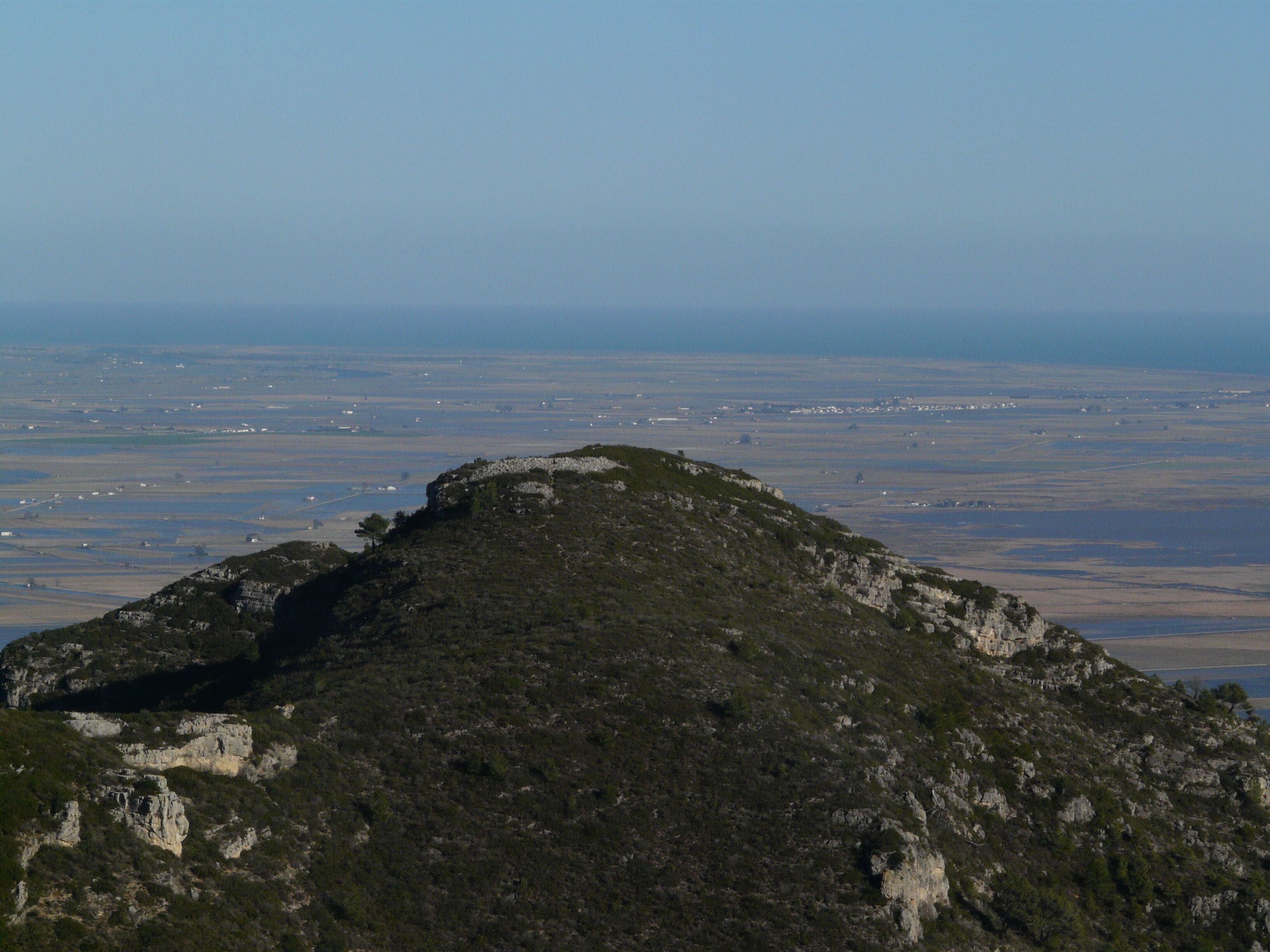 Una colina rocosa con vegetación escasa y un extenso paisaje llano al fondo.