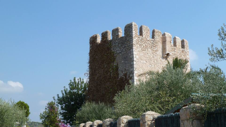 A stone castle with battlements, surrounded by greenery and a metal gate.