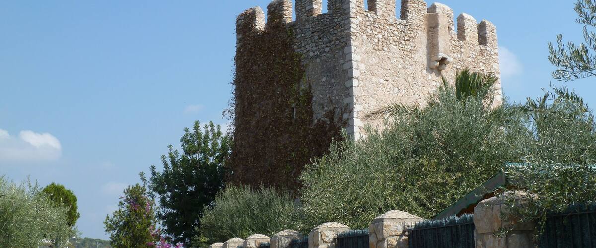 A stone castle with battlements, surrounded by greenery and a metal gate.