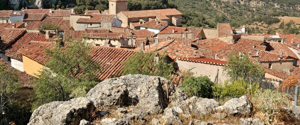 A town with red-tiled roofs, a prominent tower, and a mountainous backdrop.