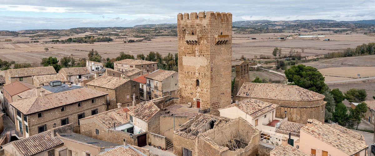 A historic town with a prominent tower, terracotta-roofed buildings, and expansive fields in the background.