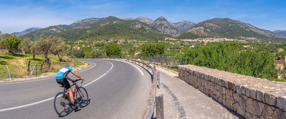 A cyclist on a winding road with mountains in the background.