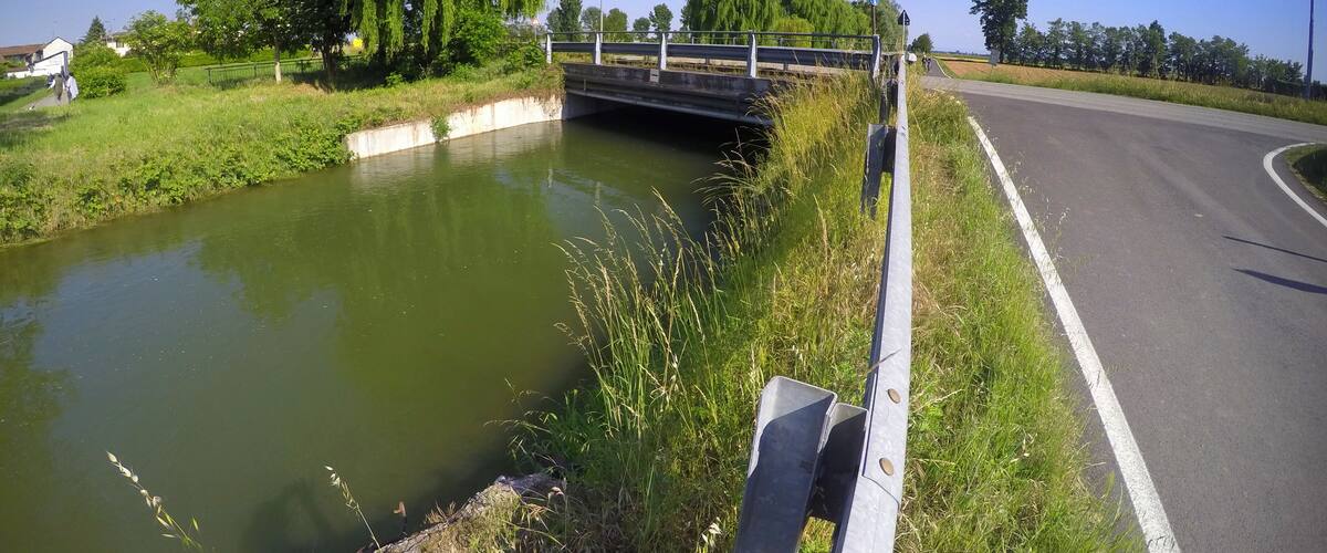 A canal with a bridge, a road, and greenery.