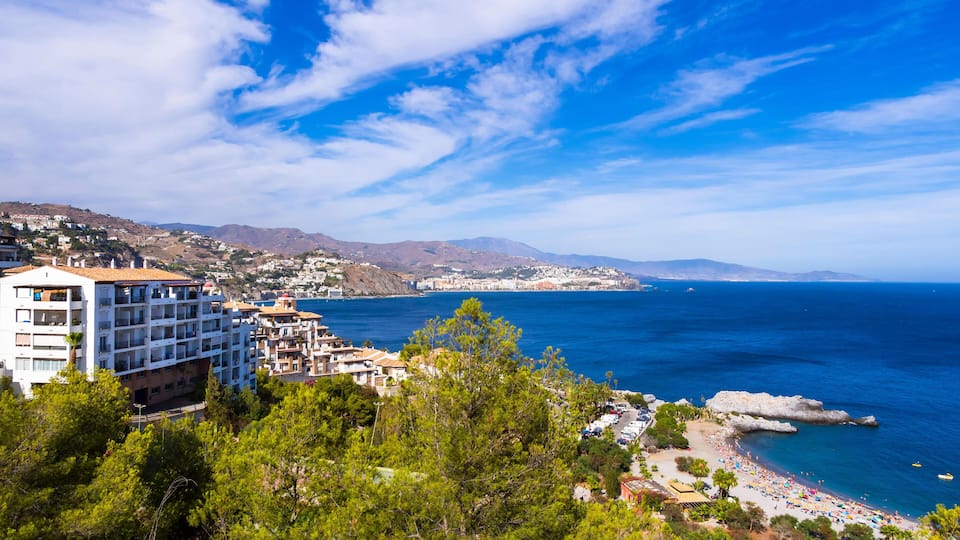 A coastal town with a beach, buildings, and mountains in the background.