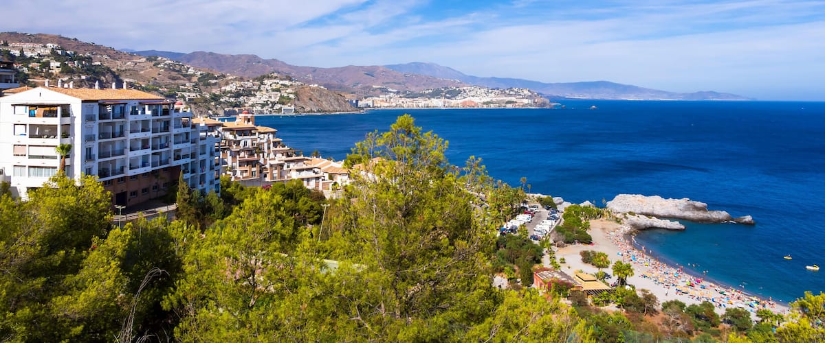 A coastal town with a beach, buildings, and mountains in the background.