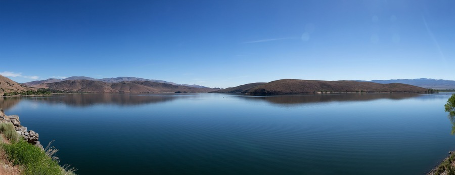 Un lago tranquilo rodeado de montañas bajo un cielo azul despejado.